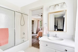A bathroom with a glass shower enclosure, a white sink with a mirror, and a ceiling fan.