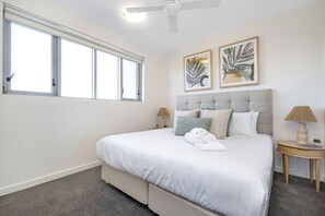 A bedroom with a large bed, two bedside lamps, a ceiling fan, and two framed artworks on the wall.