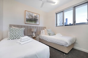 Une chambre d’hôtel avec deux lits, une vue sur la ville, un ventilateur de plafond et un tableau encadré au mur.