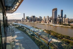 A modern building with a glass exterior, a river in the background, and a city skyline. - 2BR South Brisbane | Free Parking + Walk to QPAC (South Brisbane)
