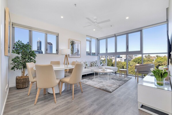 Un salon moderne avec un coin repas, de grandes fenêtres et une vue sur la ville.