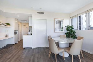 A modern dining area with a round table, four chairs, a potted plant, and a framed artwork on the wall. - 2BR South Brisbane | Free Parking + Walk to QPAC (South Brisbane)