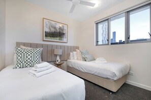 Une chambre d’hôtel avec deux lits, une vue sur la ville, un ventilateur de plafond et un tableau encadré au mur.