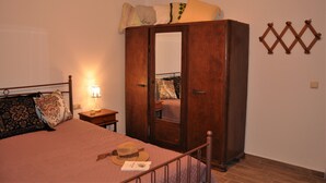 A bedroom with a bed, a wardrobe, a bedside table with a lamp, and a wall decoration. - Holiday Home 'House For Rent In Apostolous' with Mountain View, Private Garden and Wi-Fi (Iraklio)