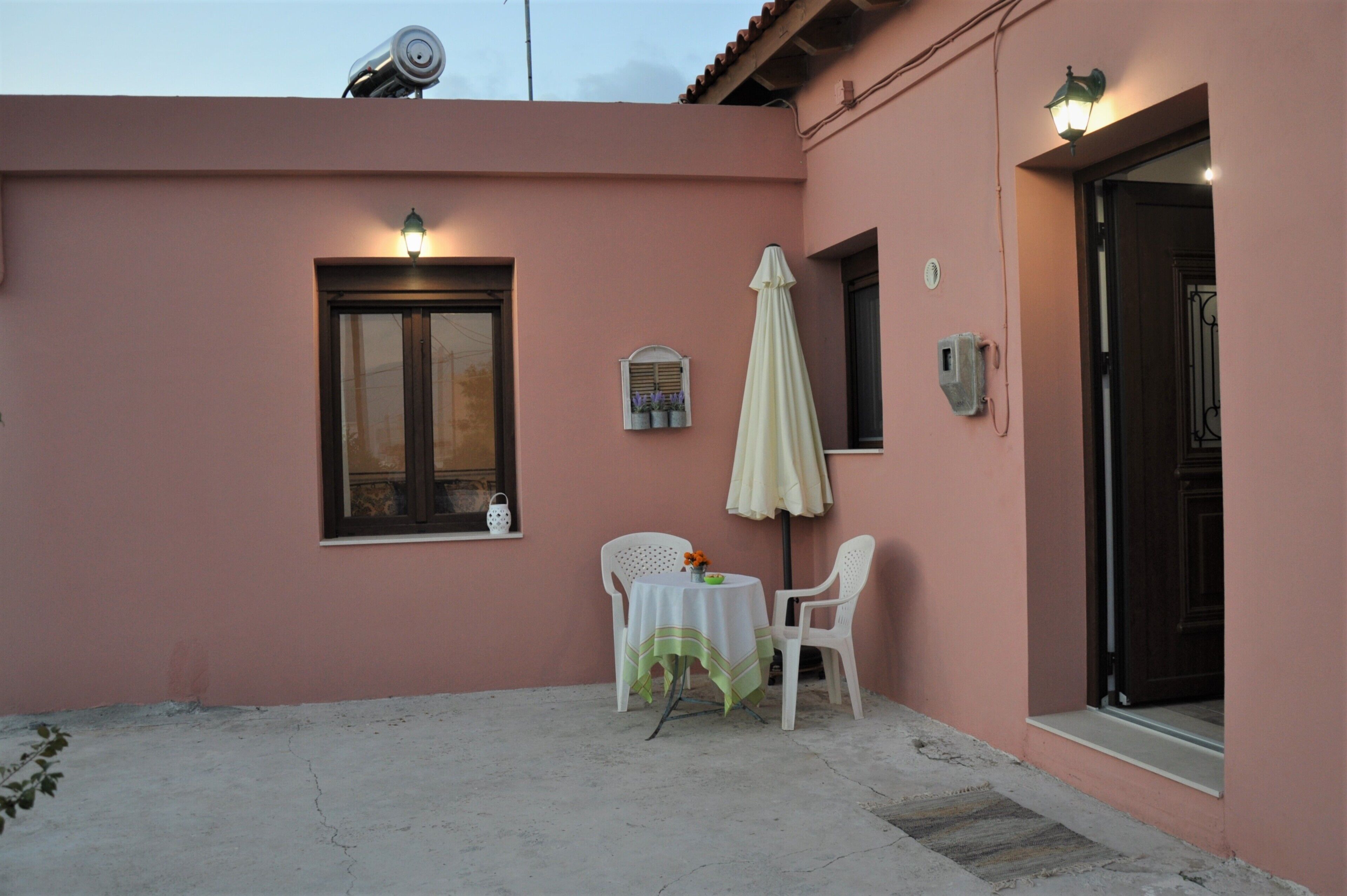 A pink building exterior with a window, a table with chairs, and a covered outdoor area.