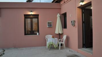 A pink building exterior with a window, a table with chairs, and a covered outdoor area.