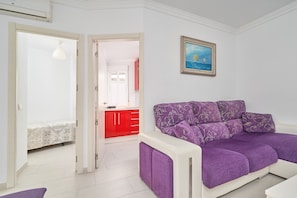 A room with a purple sofa, a painting of a sailboat, and a red cabinet in the background.