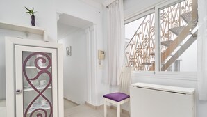 A room with a white cabinet, a chair with a purple cushion, a white radiator, and a staircase with a wrought iron railing.