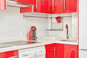 A modern kitchen with red cabinets, a white countertop, a coffee machine, and a dishwasher.