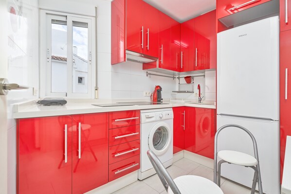 A modern kitchen with red cabinets, a white washing machine, and a compact refrigerator.