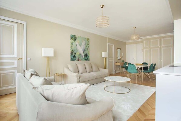 Una sala de estar con sofá, sillón y mesa de centro, un comedor con sillas y una cocina con armarios.