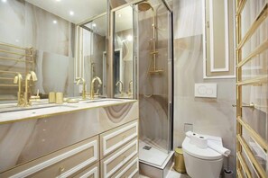 Un baño moderno con un espejo grande, accesorios dorados y una ducha con mampara de vidrio.