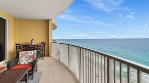 A balcony with a view of the ocean, a table with chairs, and a sofa with a floral cushion. - Emerald Isle 1709 - Beachfront condo! Front row beach chairs included! (Panama City Beach)