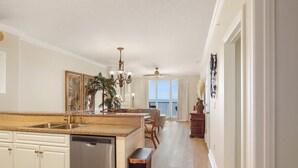 A kitchen with a dishwasher, a dining area with a table and chairs, and a view of the ocean through large windows.
