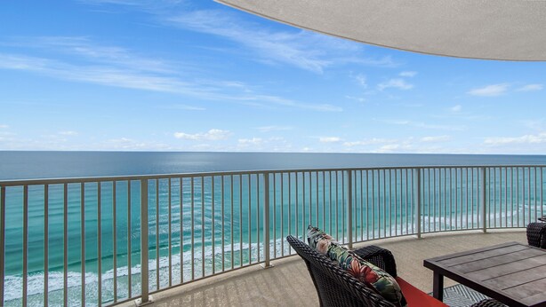 A balcony with a view of the ocean, a wicker chair, and a table.