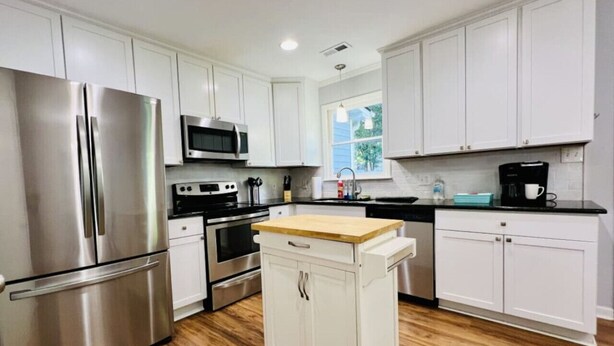 A modern kitchen with stainless steel appliances, white cabinetry, and a wooden countertop island. - Spacious Raleigh Retreat | Near Downtown + I-440 (Raleigh)