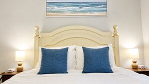 A bed with a headboard, two blue pillows, two bedside lamps, and a framed picture of the ocean on the wall. - Spacious Raleigh Retreat | Near Downtown + I-440 (Raleigh)