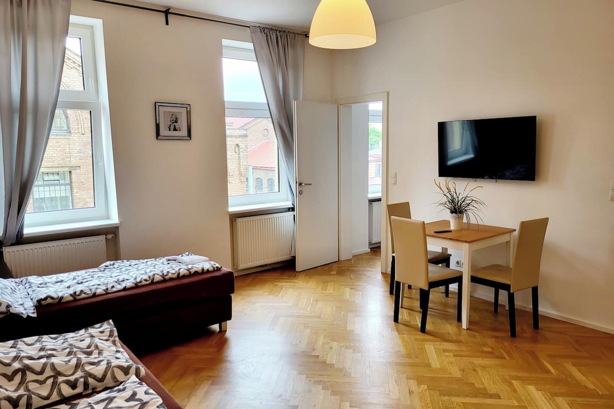 A modern bedroom with a bed, a desk with chairs, a television, and a window with curtains.