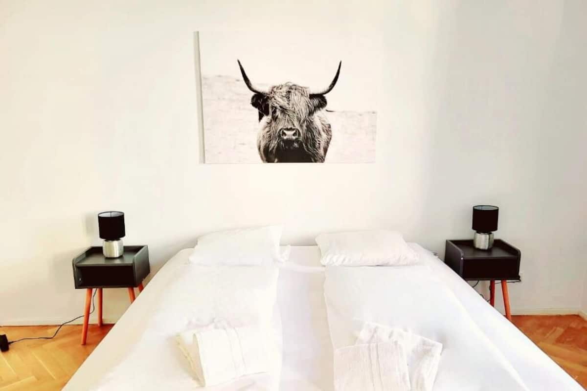 A neatly made bed with white linens, two bedside tables with lamps, and a bull-themed artwork on the wall.