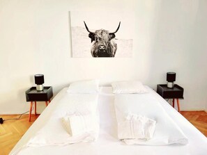 A neatly made bed with white linens, two bedside tables with lamps, and a bull-themed artwork on the wall. - City Home (Vienna)