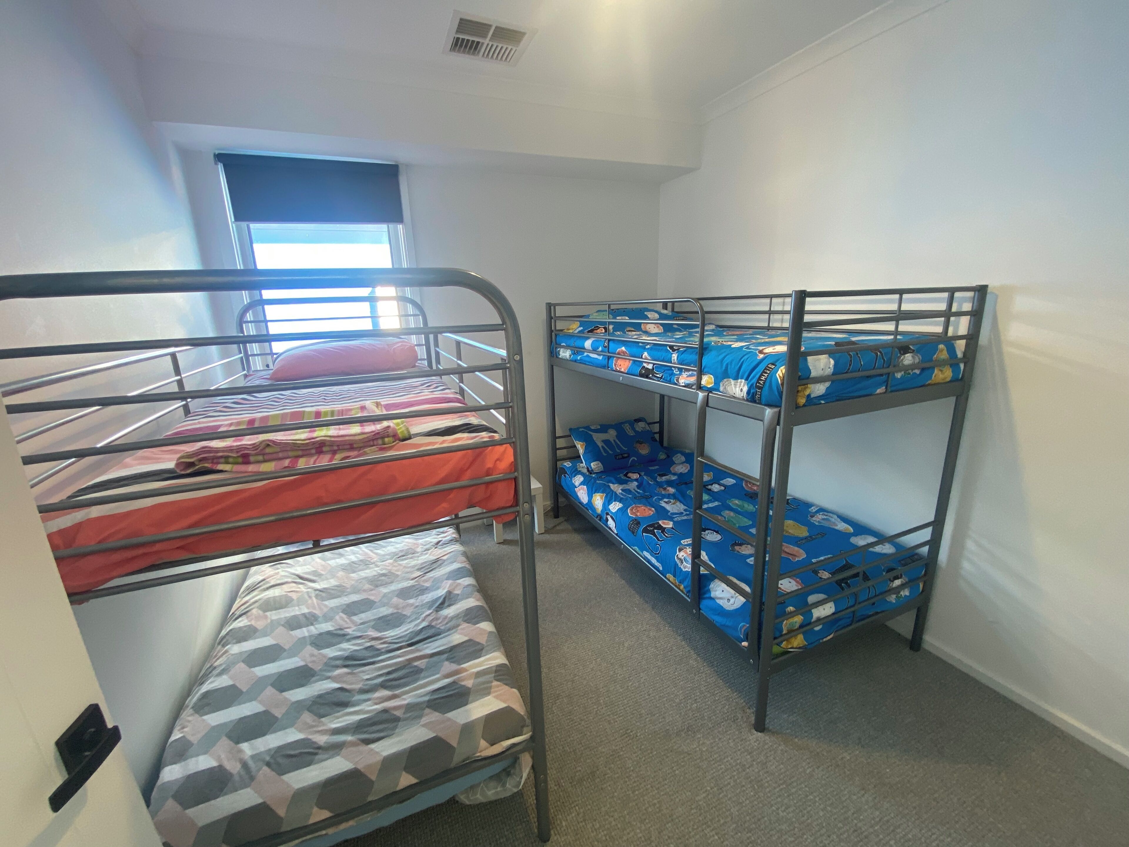 A dormitory room with bunk beds, a window, and a door.