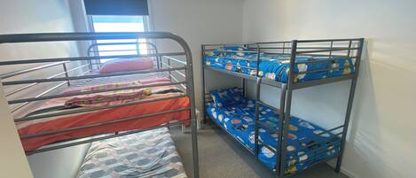 A dormitory room with bunk beds, a window, and a door.