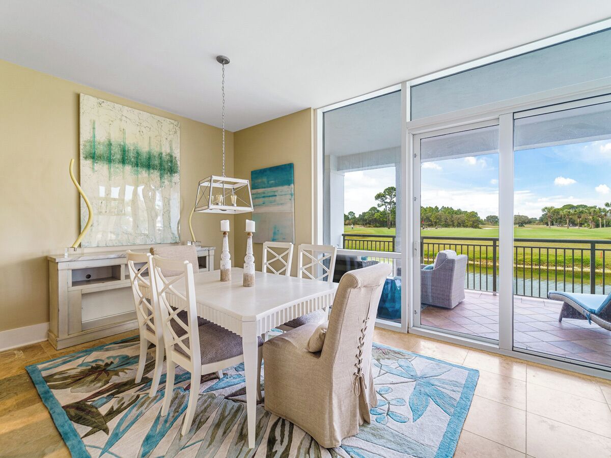 Un coin repas avec une table et des chaises blanches, une grande fenêtre donnant sur un terrain de golf et un tableau accroché au mur.