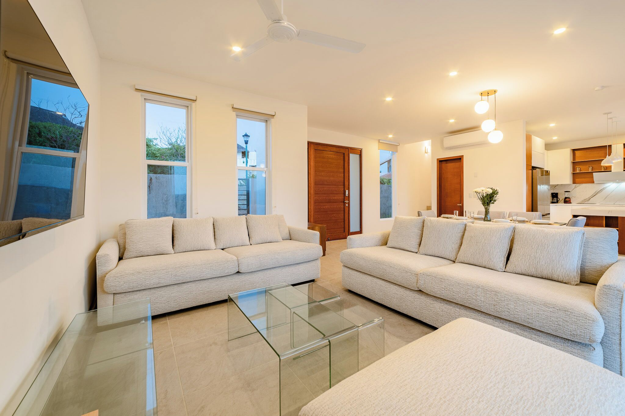 A modern living room with two sofas, a glass coffee table, and a kitchen area visible through an open door.