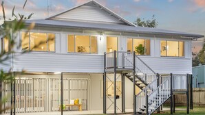 A two-story house with a covered patio area, a staircase leading to a deck, and a fenced backyard. - Luxury Waterfront Home (Evans Head)