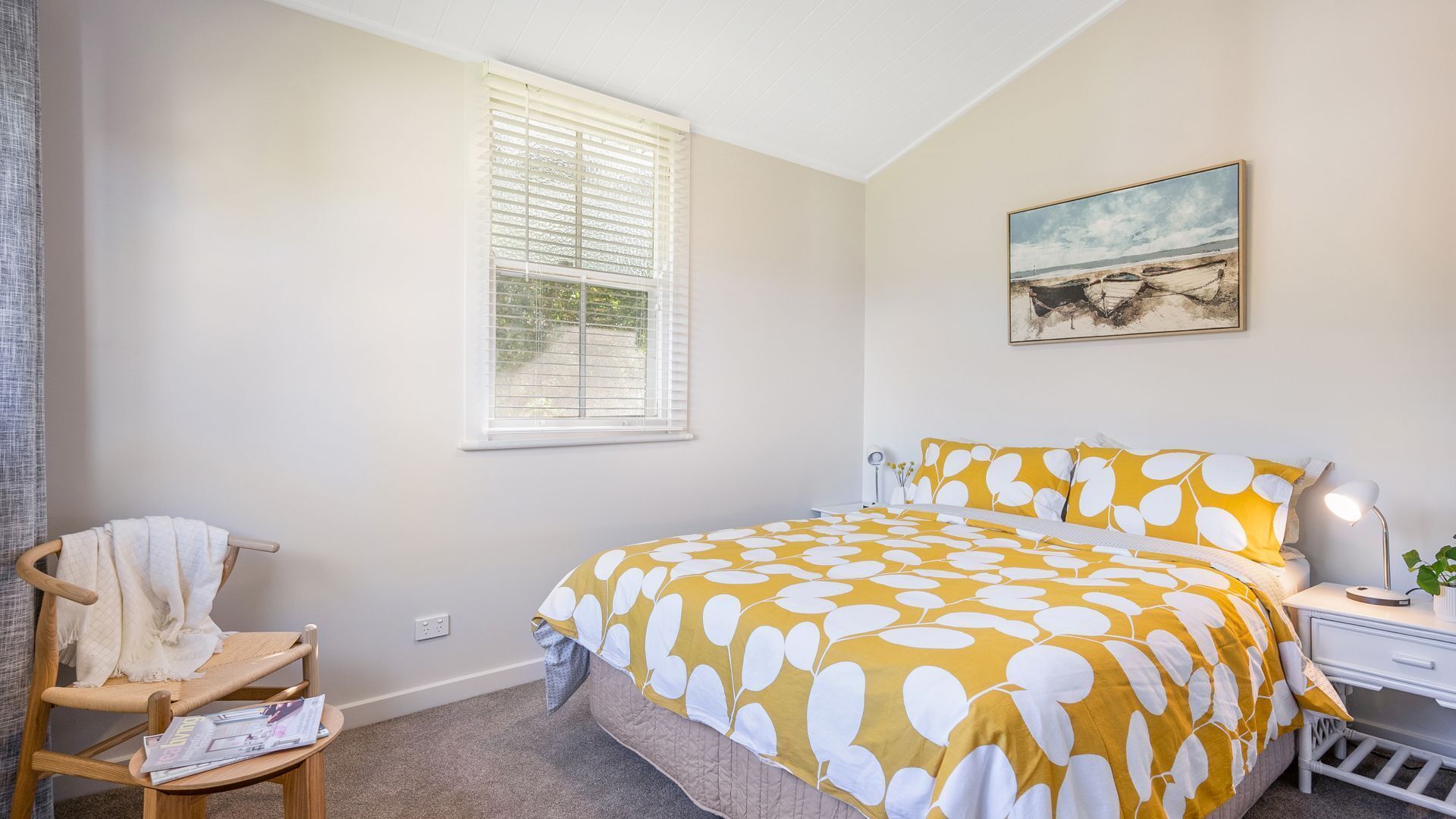 A bedroom with a bed, a chair, a desk, a window with blinds, and a painting on the wall.