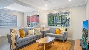 A modern living room with two grey sofas, a wooden coffee table, and a TV on a stand. - Luxury Waterfront Home (Evans Head)