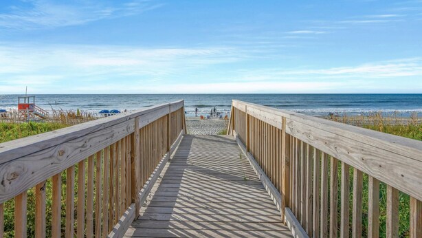 A wooden boardwalk leading to a beach with a lifeguard tower visible in the distance. - Spacious 2 bedroom unit overlooking the ocean! | Blue Water Keyes -  1108 (North Myrtle Beach)