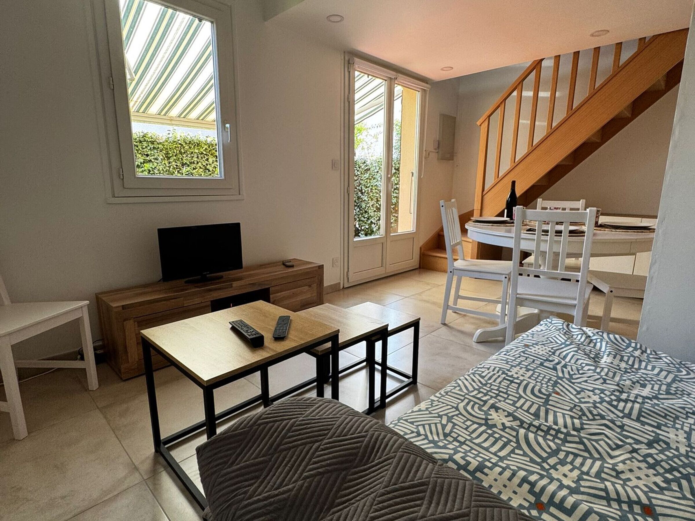A modern living room with a TV, wooden furniture, a staircase, and large windows.