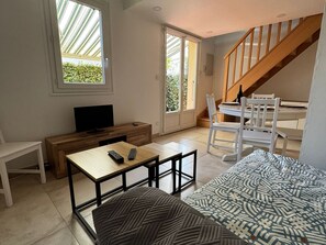 A modern living room with a TV, wooden furniture, a staircase, and large windows. - Single-storey house in Argelès-sur-Mer with garage, near transport and shops (Argelès-sur-Mer)
