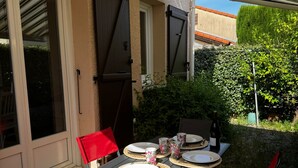 An outdoor dining area with a table set for two, surrounded by red chairs, and a bottle of wine on the table. - Single-storey house in Argelès-sur-Mer with garage, near transport and shops (Argelès-sur-Mer)