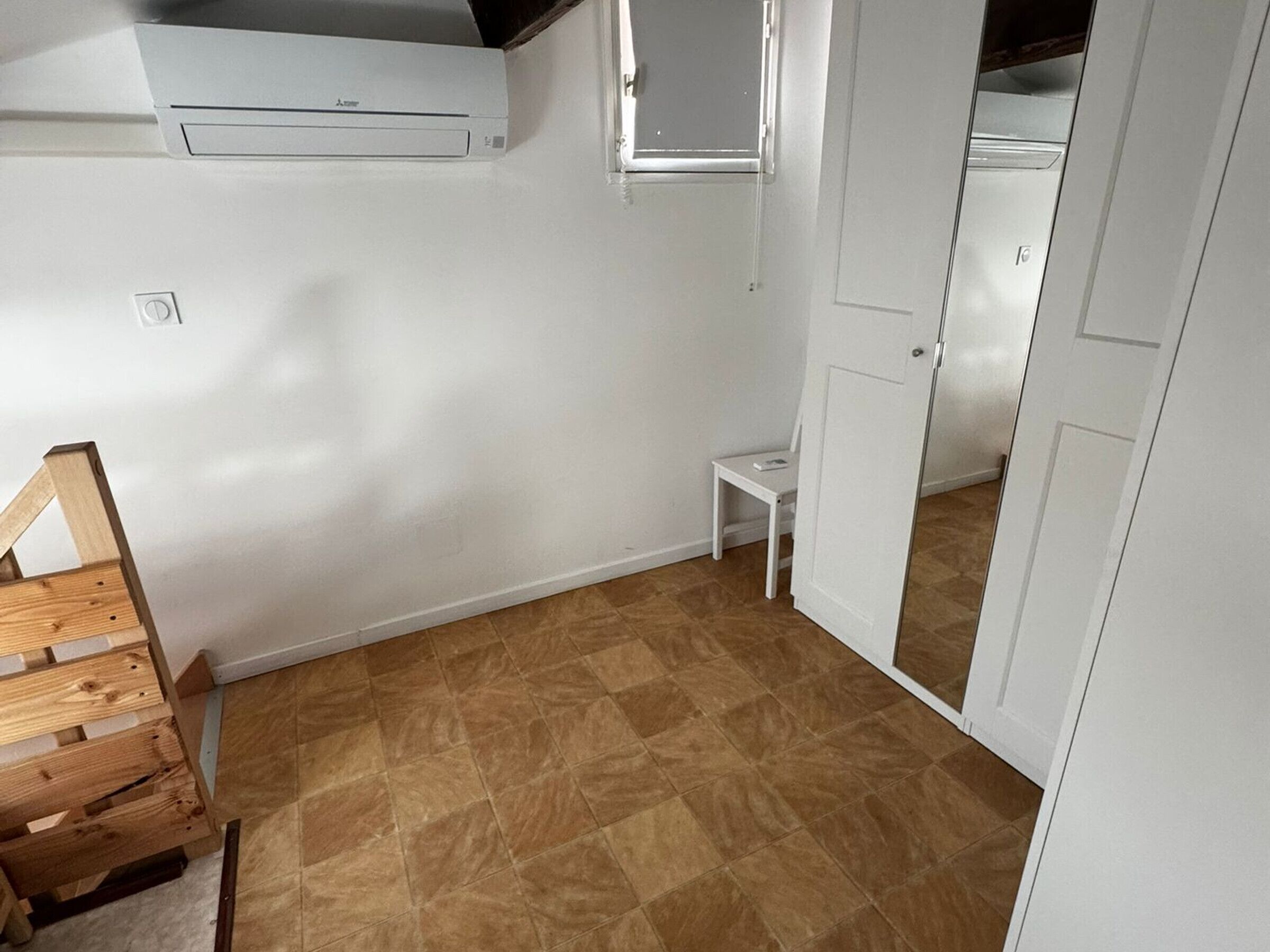 Una stanza con una panca in legno, un tavolino bianco, un armadio bianco e un pavimento piastrellato.