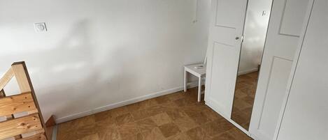 Una stanza con una panca in legno, un tavolino bianco, un armadio bianco e un pavimento piastrellato.