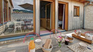 Una baita in legno con un patio, un tavolo da pranzo, sedie e un angolo cottura con una caffettiera e tazze.