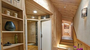 Un interno in legno con un corridoio che conduce a una camera da letto. Si vedono scaffali con diversi oggetti, una porta e una scala.