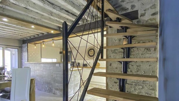 A modern interior with exposed brick walls, a wooden staircase, and a kitchen area with a bar. - Charming old house in the heart of the village with garden and terrace (Rouperroux)