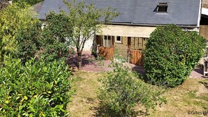 A traditional house with a sloped roof, a small attached wooden structure, and a garden with various plants and shrubs. - Charming old house in the heart of the village with garden and terrace (Rouperroux)