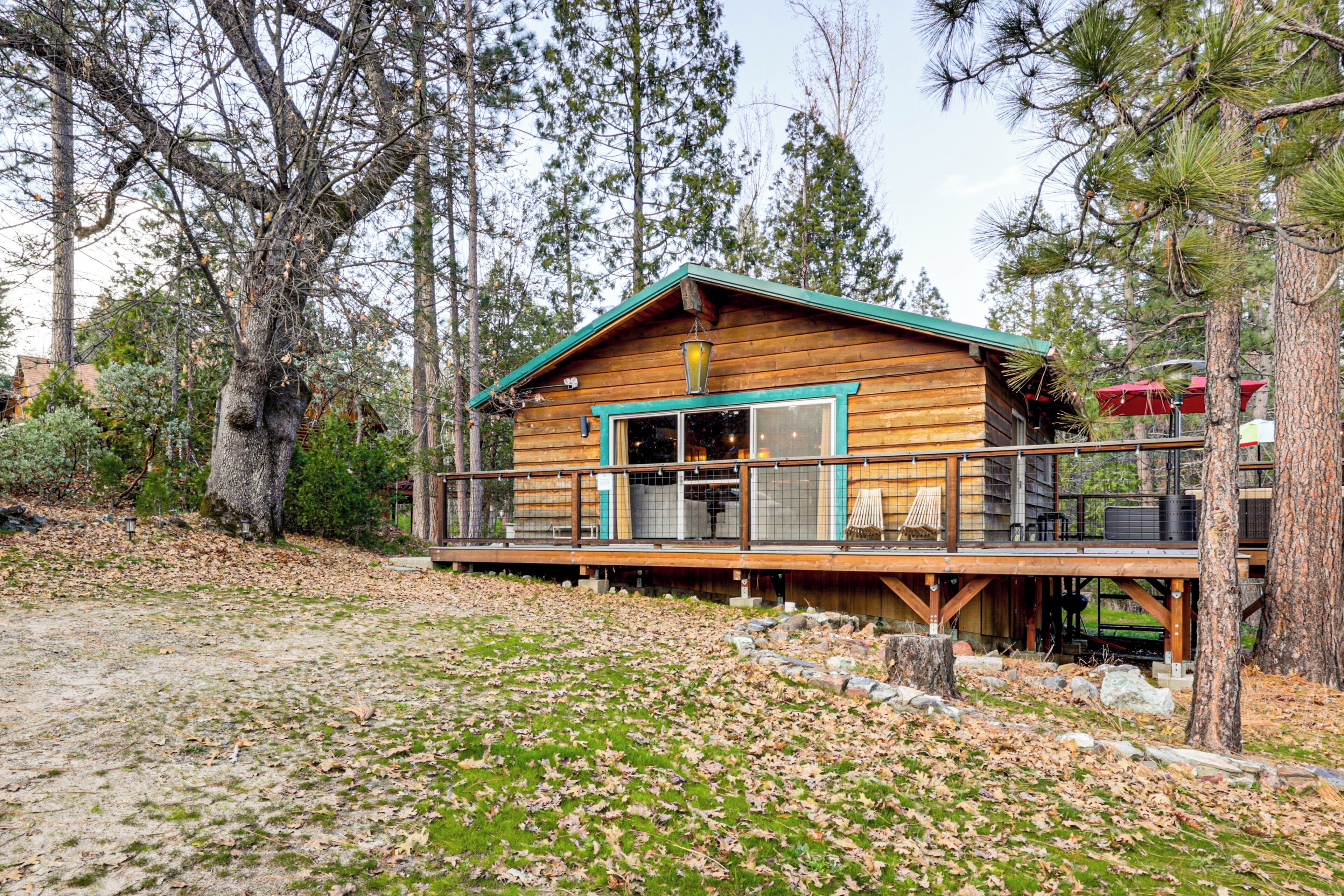 A wooden cabin with a deck, surrounded by trees.
