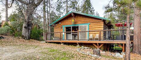 A wooden cabin with a deck, surrounded by trees.