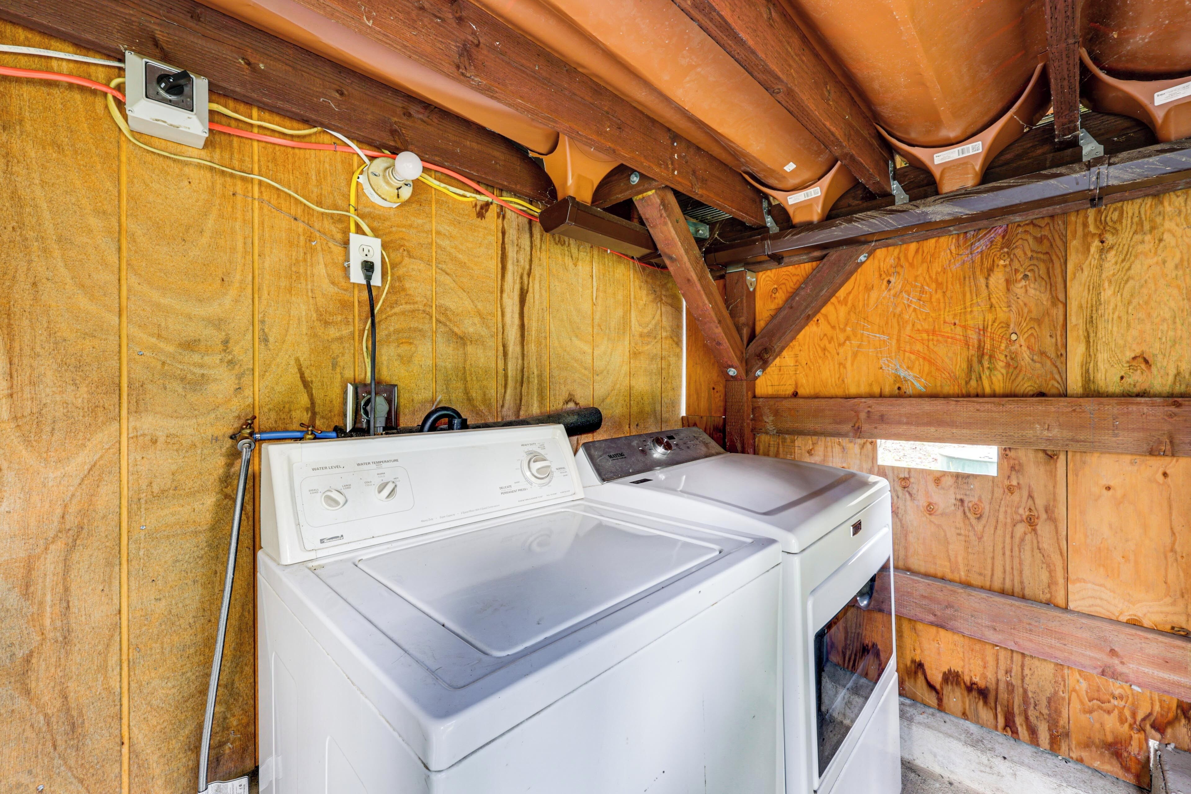 Un cuarto de lavandería con dos lavadoras y secadoras apiladas, paredes de madera y cableado eléctrico a la vista.