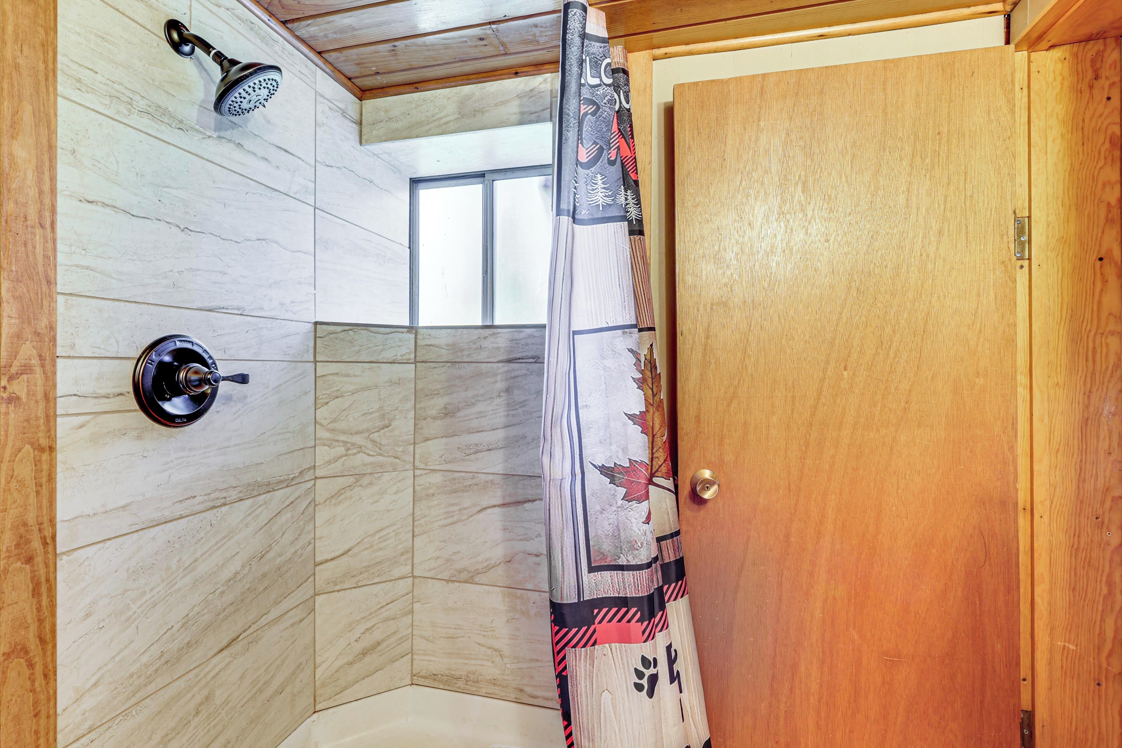 A corner shower with a wooden door, a showerhead, and a window.