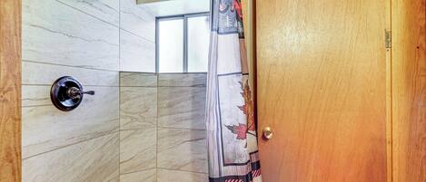 A corner shower with a wooden door, a showerhead, and a window.