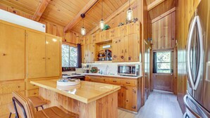 A wooden cabin kitchen with a central island, bar stools, a microwave, and a refrigerator. - Peaceful Wooden Cabin, 2 Mi to Bass Lake! (Oakhurst)