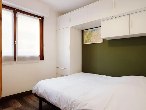 Ein Schlafzimmer mit Bett, Kleiderschrank, einer Karte an der Wand und einem Fenster mit Vorhängen.