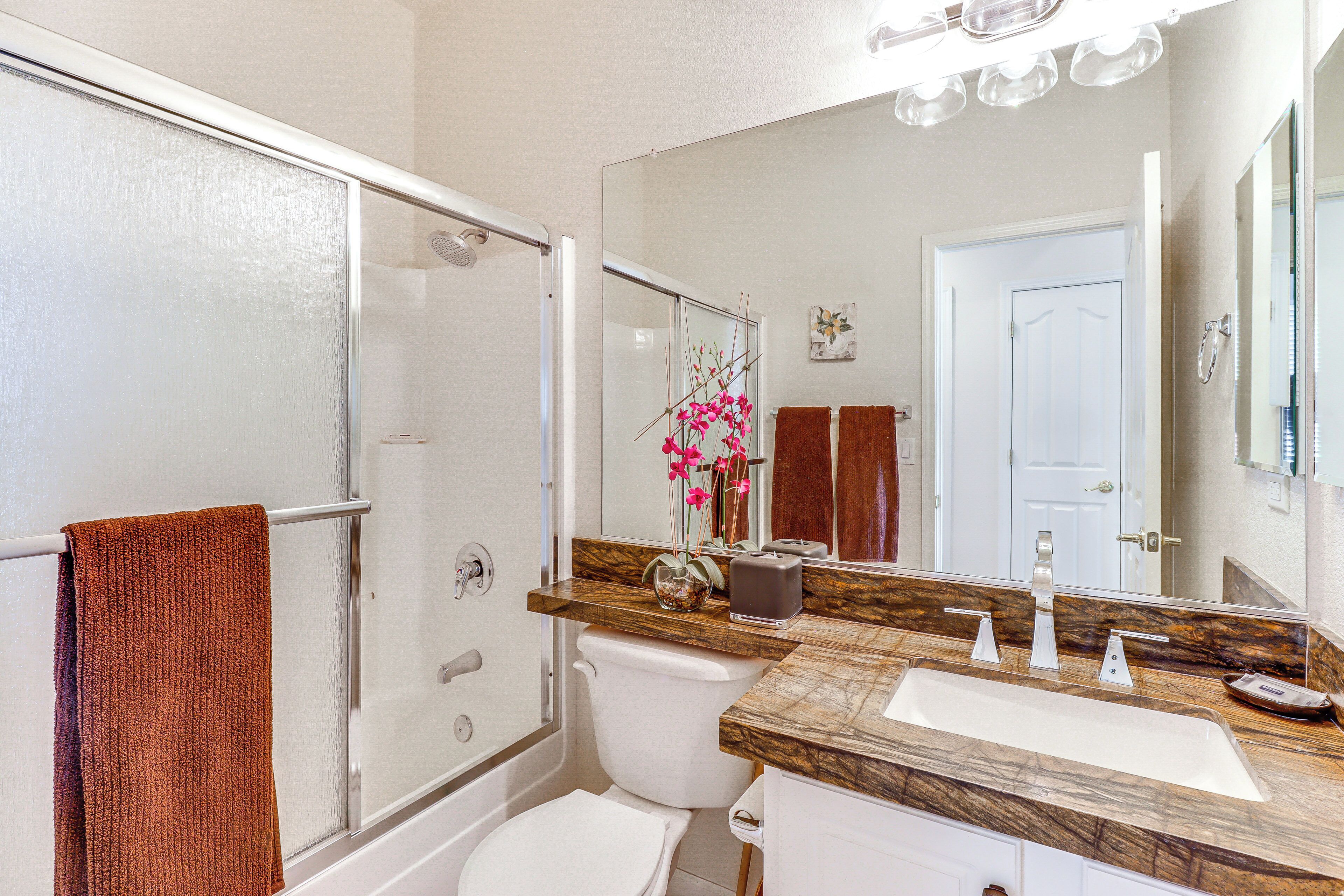 A bathroom with a glass shower enclosure, a white toilet, a vanity with a marble countertop, and a large mirror.