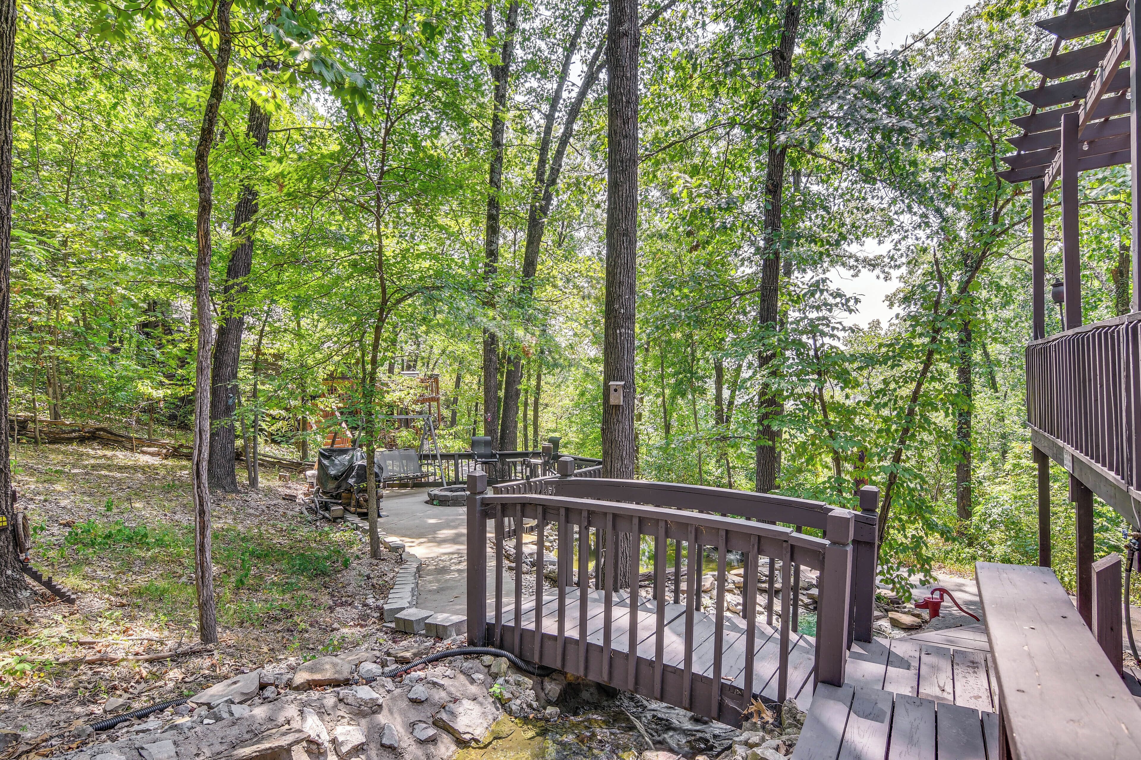 A wooden deck with a railing, surrounded by trees and a stone pathway.